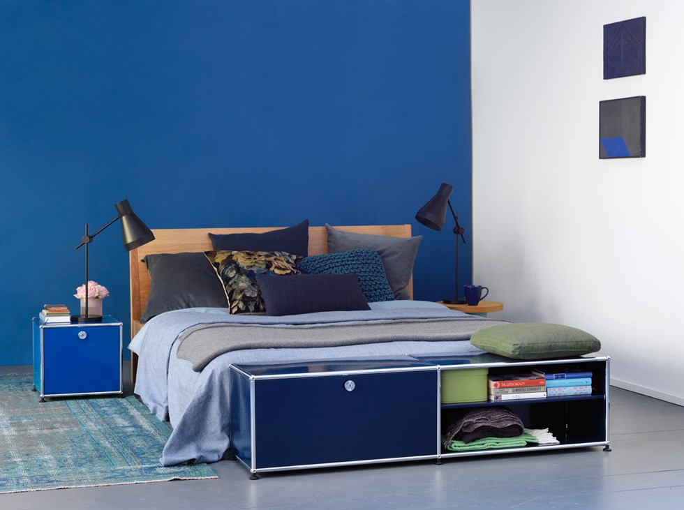 USM haller blue end of bed storage in dark walled bedroom