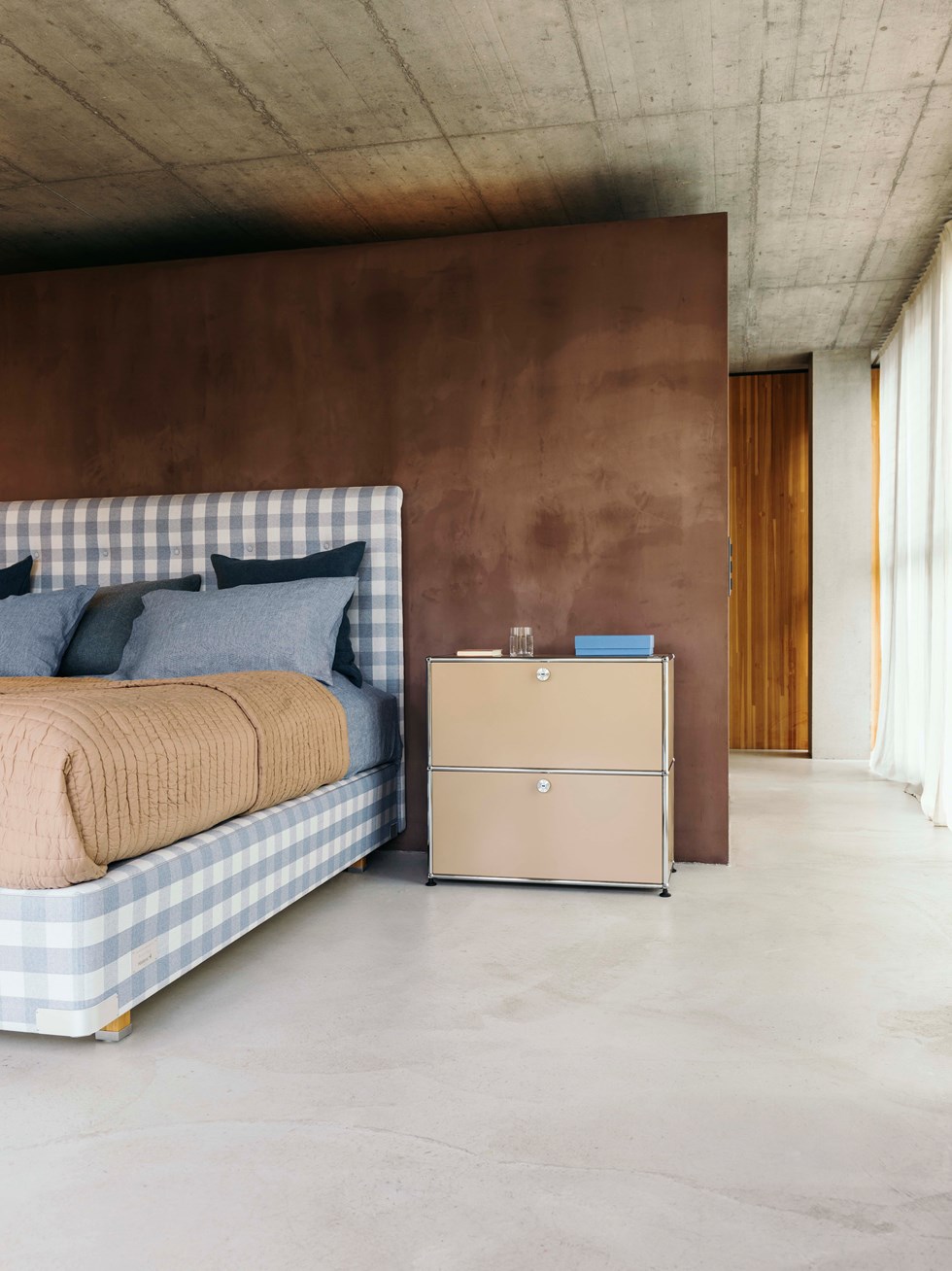 Comodino con cassetti beige USM Haller in una camera da letto con pavimento in cemento